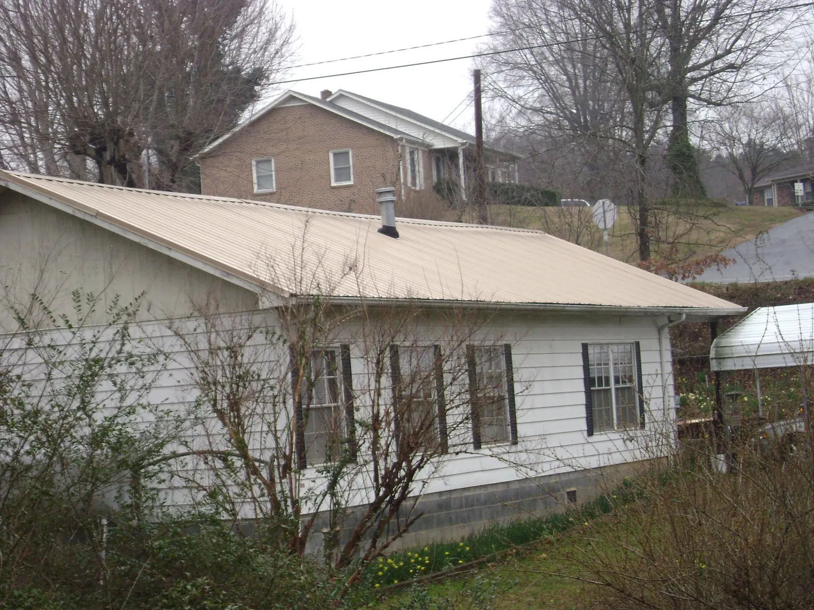 Tan metal roof on a white sided house set into a hillside — Commercial Roofing by Roofing Brothers in Ansonia